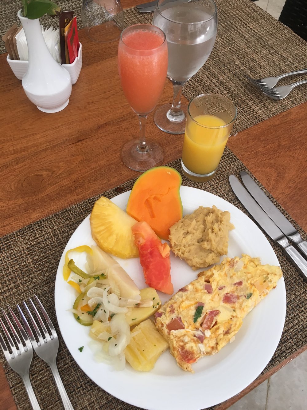 A vibrant plate featuring a colorful omelette, fresh papaya, pineapple slices, and a scoop of mashed plantains, paired with a glass of orange juice and a pink smoothie, exemplifying allergen-friendly, nourishing meals with fresh flavors.| Daré Vita Café | Las Vegas