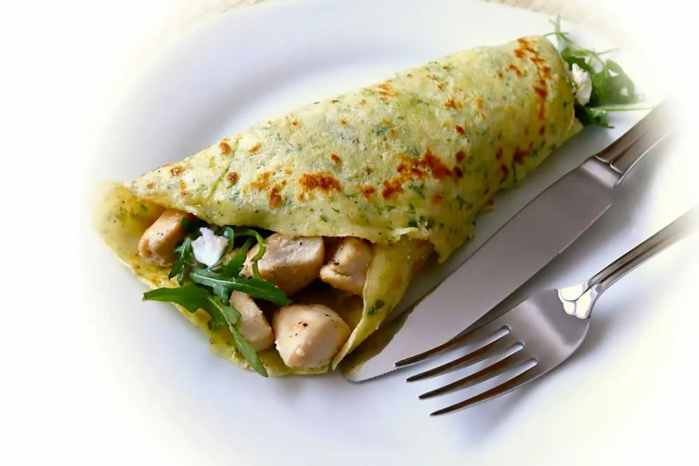 carousel-11 A vibrant, gluten-free crepe filled with fresh chicken pieces and arugula, resting on a white plate with a fork and knife beside it, showcasing a wholesome, allergen-friendly meal with clean ingredients.| Daré Vita Café | Las Vegas