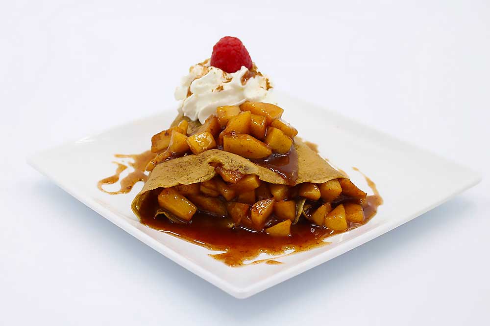 A vibrant, gluten-free crepe filled with spiced apples, topped with a dollop of whipped cream and a fresh raspberry, showcasing allergen-friendly, wholesome ingredients on a white plate.| Daré Vita Café | Las Vegas