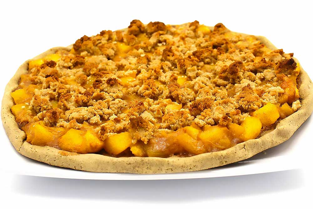A vibrant, gluten-free peach crumble pie on a white plate, featuring a golden, crumbly topping and juicy peach filling. This wholesome dessert is made with natural, minimally processed ingredients, perfect for those seeking allergen-friendly options.| Daré Vita Café | Las Vegas