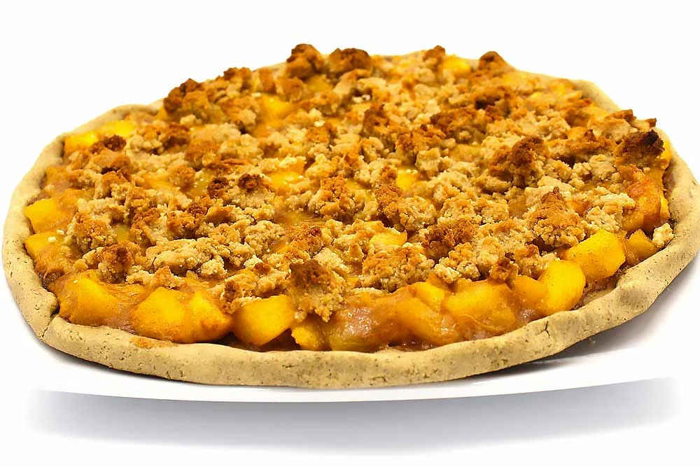 A vibrant, gluten-free peach crumble pie on a white plate, featuring a golden, crumbly topping and juicy peach filling. This wholesome dessert is made with natural, minimally processed ingredients, perfect for those seeking allergen-friendly options.| Daré Vita Café | Las Vegas