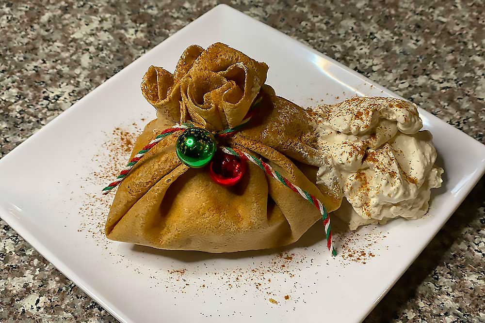 A vibrant, allergen-friendly crepe pouch tied with colorful string, garnished with whipped cream and cinnamon, sits on a white plate. The dish is designed to be nourishing and made with fresh, natural ingredients.| Daré Vita Café | Las Vegas