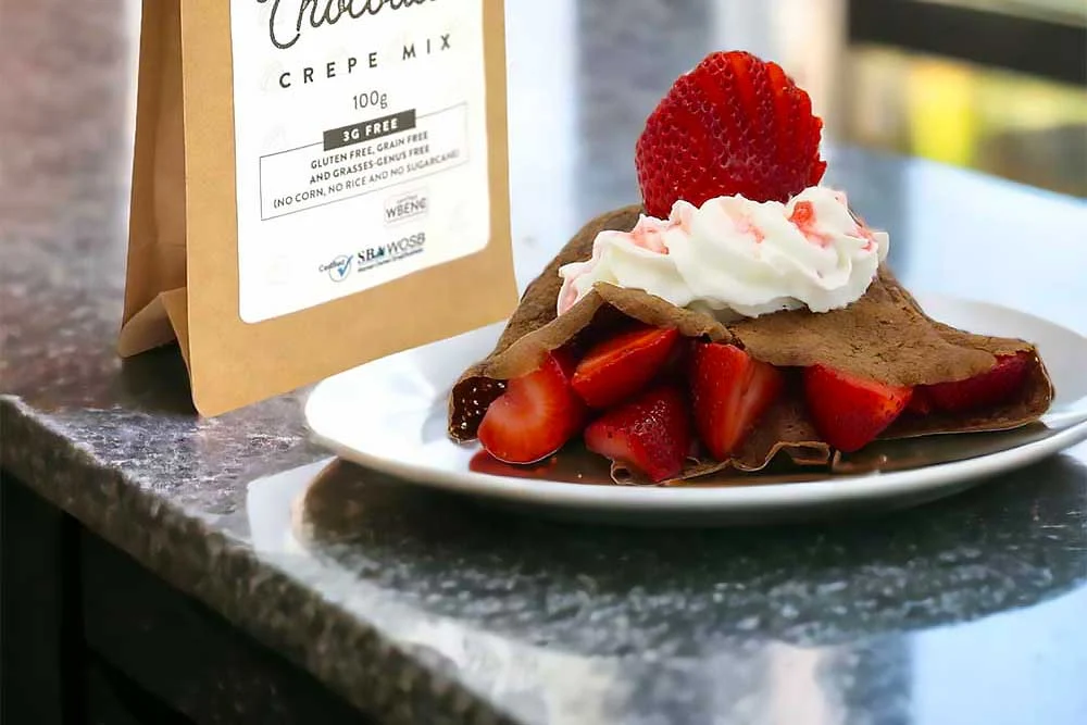 A plate with a vibrant, allergen-friendly chocolate crepe filled with fresh strawberries and topped with whipped cream sits next to a bag labeled gluten-free crepe mix, emphasizing natural, wholesome ingredients.| Daré Vita Café | Las Vegas