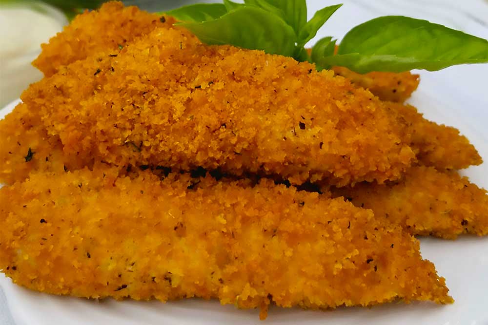 Crispy, golden, plant-based tenders on a white plate, garnished with fresh basil leaves, showcasing a delicious, allergen-friendly option made with minimal processing for a nourishing, vibrant meal.| Daré Vita Café | Las Vegas