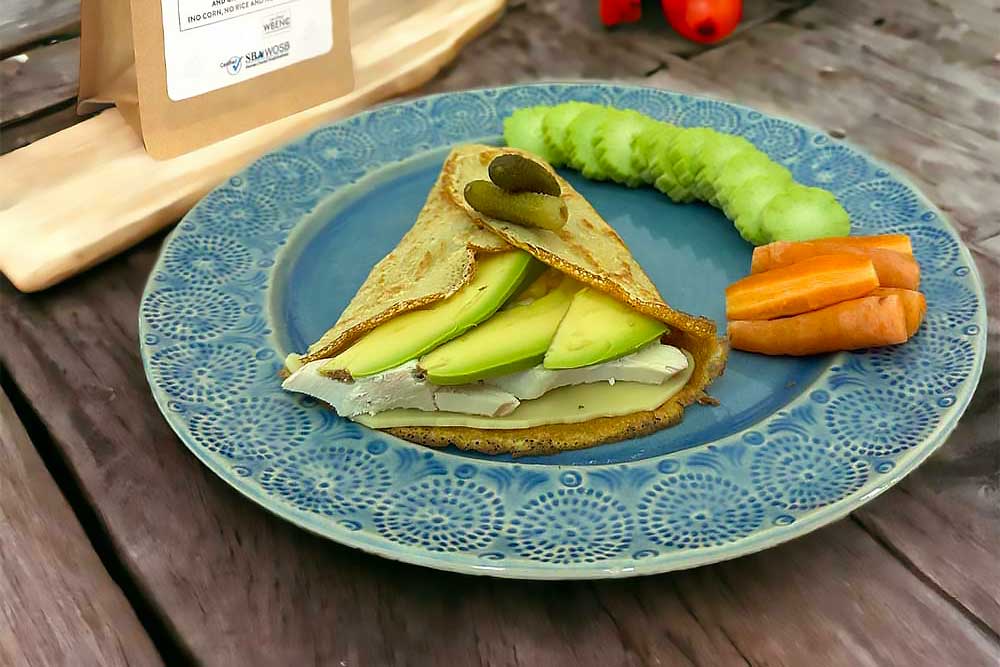 A vibrant crepe filled with fresh avocado and cucumber slices sits on a blue plate, accompanied by carrot sticks and a pickle, representing a healthy, plant-based, allergen-friendly meal.| Daré Vita Café | Las Vegas