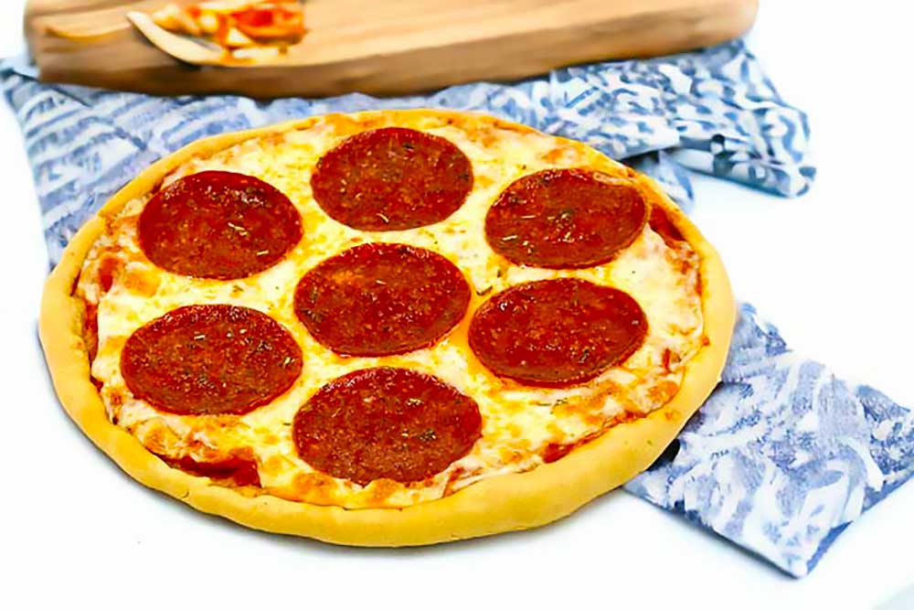 A vibrant, plant-based pepperoni pizza sits on a patterned cloth, showcasing a golden crust with plant-based pepperoni slices. This allergen-friendly, dairy-free dish highlights fresh, wholesome ingredients perfect for those with food sensitivity.| Daré Vita Café | Las Vegas