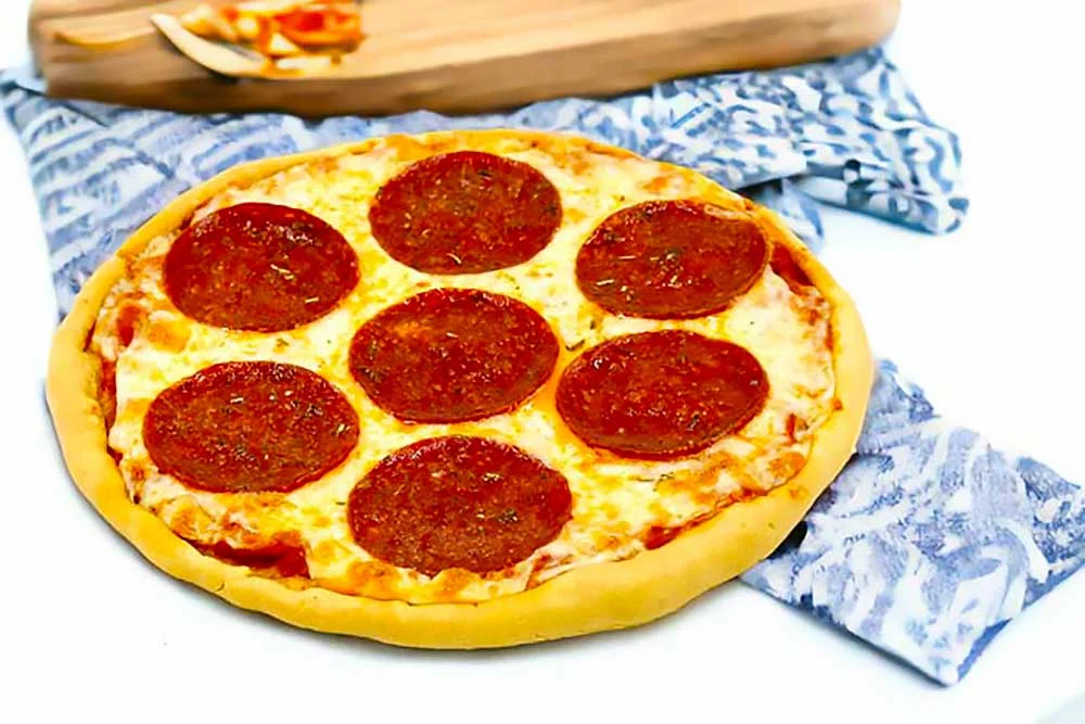 A vibrant, plant-based pepperoni pizza sits on a patterned cloth, showcasing a golden crust with plant-based pepperoni slices. This allergen-friendly, dairy-free dish highlights fresh, wholesome ingredients perfect for those with food sensitivity.| Daré Vita Café | Las Vegas