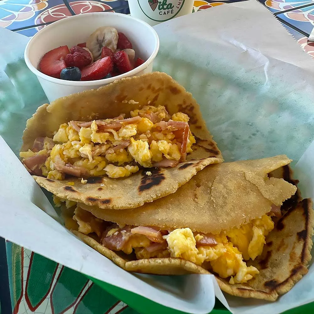 A vibrant, allergen-friendly breakfast featuring two roti wraps filled with scrambled eggs and ham, accompanied by a cup of fresh fruit, perfect for a nourishing start to the day.| Daré Vita Café | Las Vegas