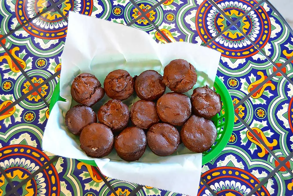 A vibrant green basket holds chocolate muffins on a colorful patterned table. These allergen-friendly treats are made with clean ingredients, perfect for those seeking natural, wholesome options.| Daré Vita Café | Las Vegas