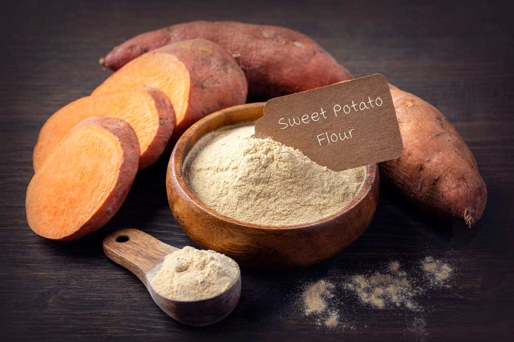sweet-potatoe-flour-image A wooden bowl filled with sweet potato flour is surrounded by fresh orange sweet potato slices and whole sweet potatoes, exemplifying allergen-friendly, gluten-free, and plant-based ingredients ideal for nourishing, wholesome meals.| Daré Vita Café | Las Vegas