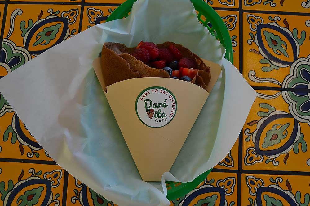 about-us-2 A vibrant, allergen-friendly crepe from Daré Vita Café filled with fresh berries, wrapped in branded paper on a colorful, decorative tile background, showcasing their commitment to healthy, wholesome meals.| Daré Vita Café | Las Vegas