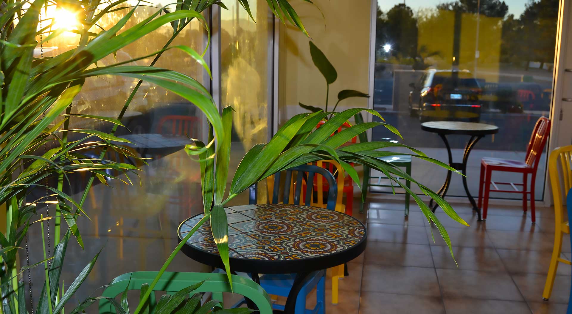 Sunlit café interior with colorful chairs and mosaic tables, surrounded by lush green plants, creating a vibrant and welcoming atmosphere perfect for enjoying allergen-friendly, plant-based meals.| Daré Vita Café | Las Vegas