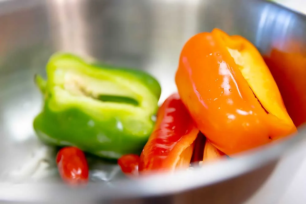 new-ingredients-3 A vibrant image of fresh green and orange bell peppers with red chili peppers in a metal bowl, showcasing natural, fresh produce ideal for creating wholesome, plant-based dishes that support healthy living and food sensitivity needs.| Daré Vita Café | Las Vegas
