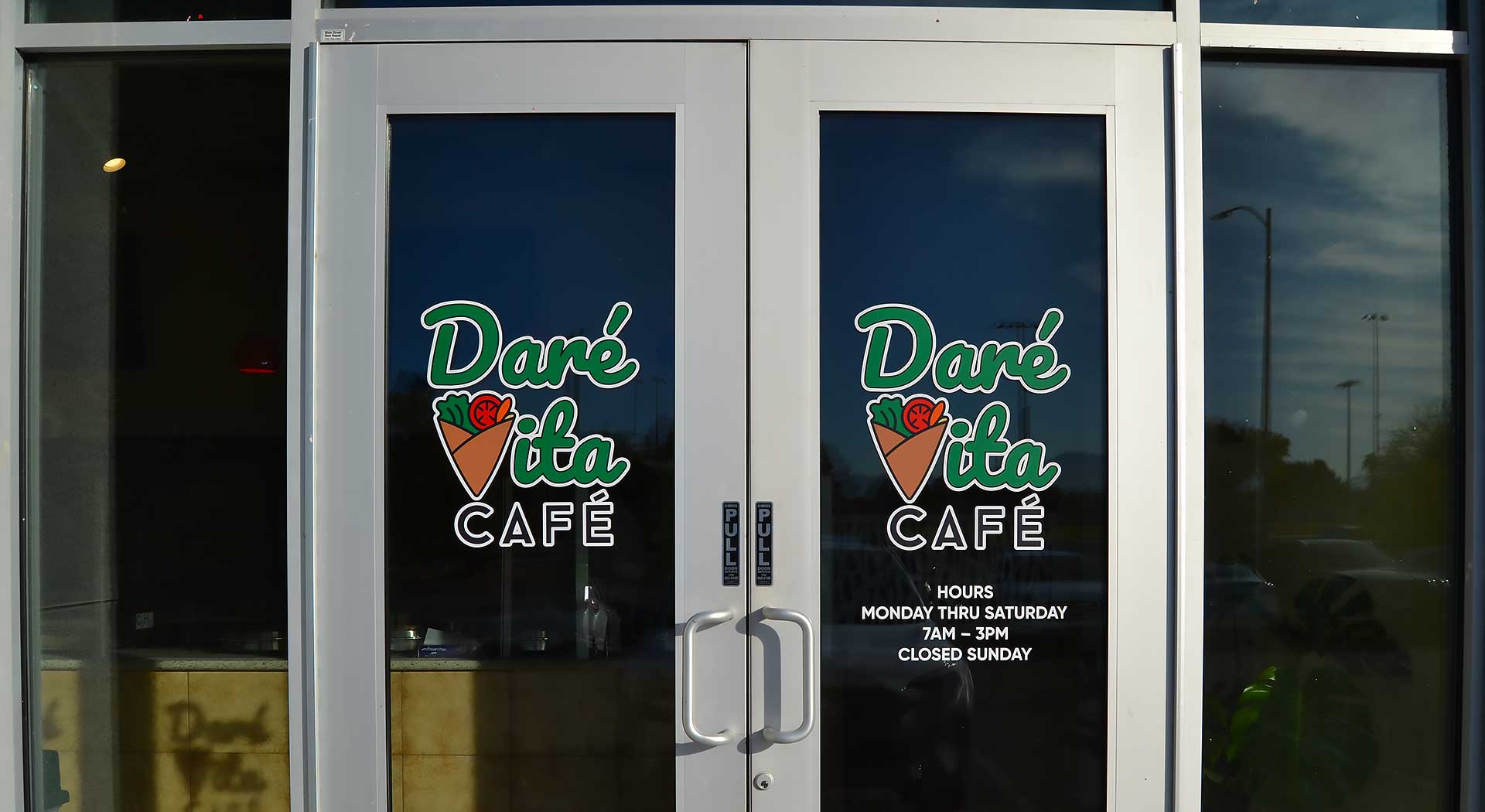 slider-image-1b Entrance of Daré Vita Café with glass doors displaying the logo in green and white. The café offers allergen-friendly, plant-based meals, emphasizing fresh, wholesome ingredients. Visible hours indicate Monday to Saturday, 7 AM to 3 PM.| Daré Vita Café | Las Vegas