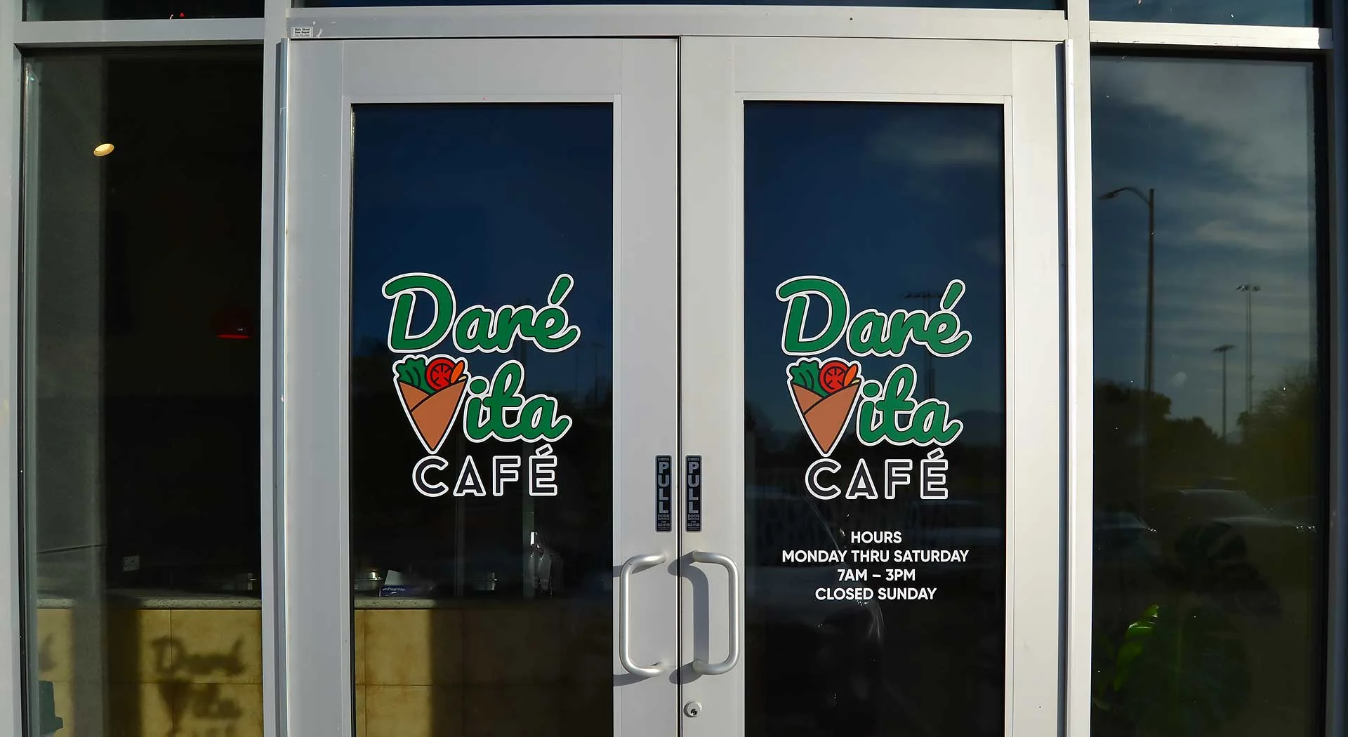 slider-image-1b Entrance of Daré Vita Café with glass doors displaying the logo in green and white. The café offers allergen-friendly, plant-based meals, emphasizing fresh, wholesome ingredients. Visible hours indicate Monday to Saturday, 7 AM to 3 PM.| Daré Vita Café | Las Vegas