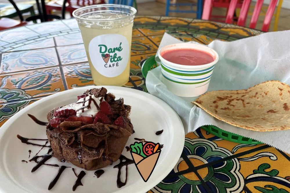 Behind the Apron_ The Heart and Vision of Dare Vita Café (2) A vibrant, allergen-friendly meal featuring a chocolate crepe topped with strawberries and whipped cream, a bowl of pink soup, a roti wrap, and a refreshing drink on a colorful tiled table at Daré Vita Café.| Daré Vita Café | Las Vegas