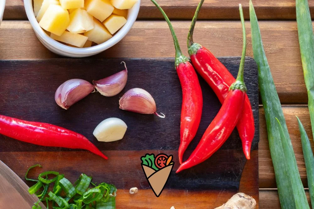 Behind the Apron_ The Heart and Vision of Dare Vita Café (3) A vibrant display of fresh produce, including red chili peppers, garlic cloves, and diced potatoes, arranged on a wooden surface. This allergen-friendly selection highlights natural,…| Daré Vita Café | Las Vegas