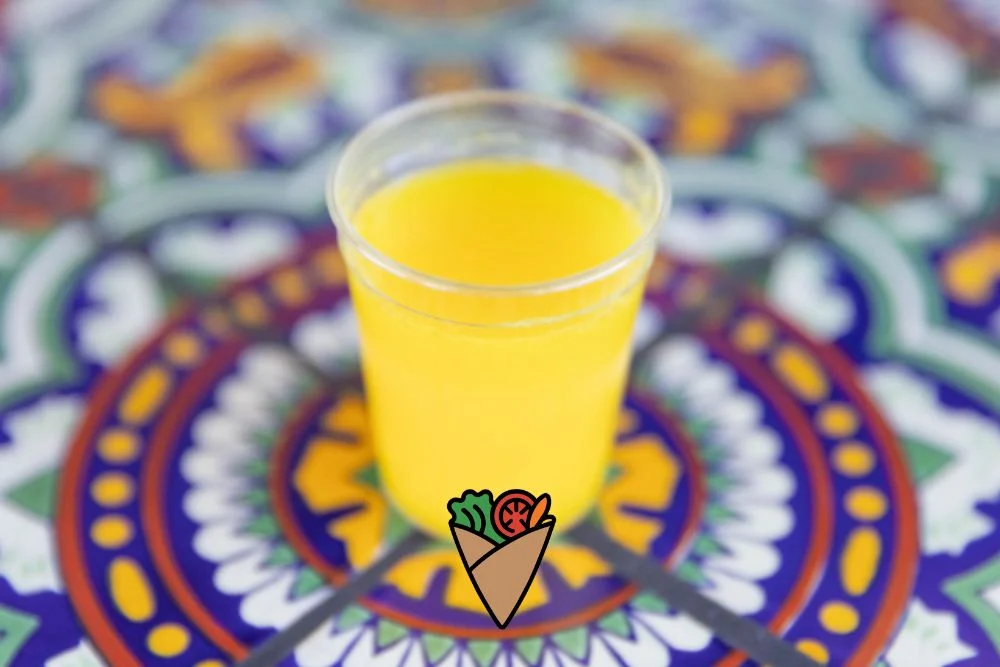 Behind the Apron_ The Heart and Vision of Dare Vita Café (6) A vibrant yellow smoothie in a clear cup sits on a colorful, patterned table. The smoothie, made with fresh, natural ingredients, offers a refreshing, allergen-friendly, and healthy option, perfect for those seeking a nourishing and wholesome drink.| Daré Vita Café | Las Vegas