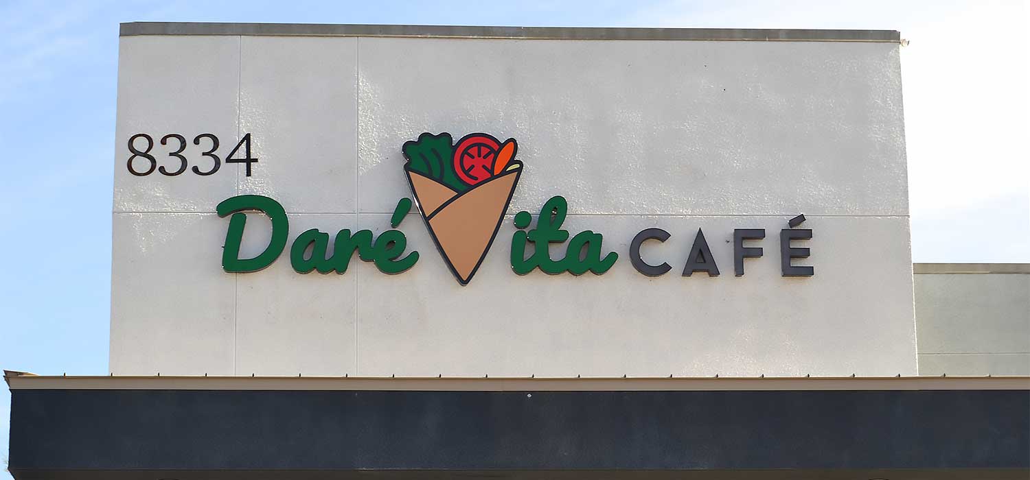 The image shows the Daré Vita Café sign with vibrant green and black lettering. The café specializes in plant-based, allergen-friendly meals with fresh ingredients, depicted by a logo of a wrap filled with colorful vegetables.| Daré Vita Café | Las Vegas