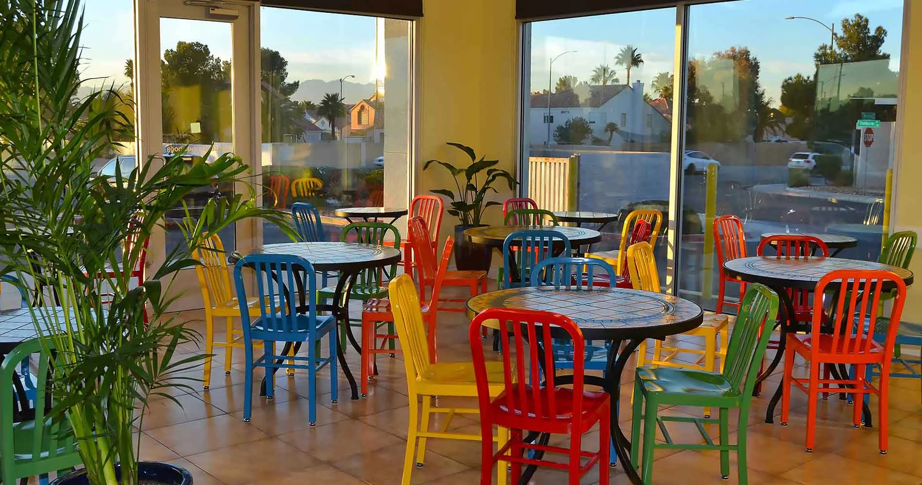 A brightly lit café interior with colorful chairs and tables, surrounded by large windows and lush plants, creating a vibrant atmosphere perfect for enjoying allergen-friendly, nourishing meals.| Daré Vita Café | Las Vegas